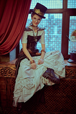 Portrait of a charming steampunk lady sitting on a windowsill in a room with Victorian vintage...