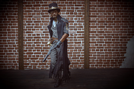 Full length portrait of a courageous steampunk male warrior running with a gun on a brickwall background. World of steampunk.の写真素材