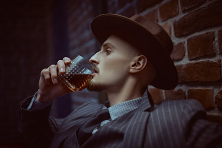 Handsome drunk man sitting relaxed in a rich setting on a leather sofa with a glass of whiskey. Luxurious lifestyle. Retro style. Mafia and criminal world.の写真素材