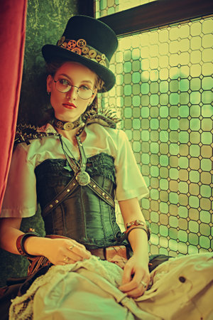 Portrait of a charming steampunk lady sitting on a windowsill in a room with Victorian vintage interior.の写真素材