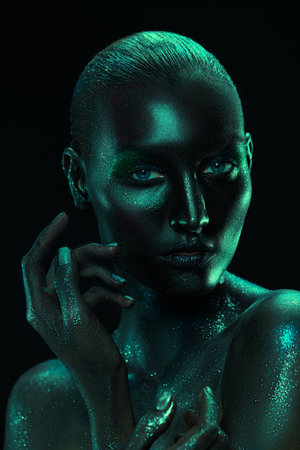 Body painting and makeup. Portrait of a beautiful fashion model woman with black painted skin and sparkling glitter makeup. Black background.の写真素材