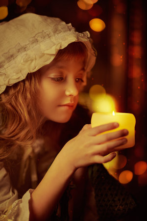 Magic time. Christmas in the old days. Cute little girl in a nightgown and a cap looks at the candle on Christmas night.の写真素材