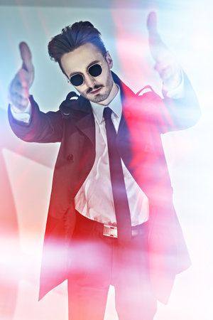 Modern stylish man in elegant black suit, white shirt and sunglasses posing on a gray background with shadows. Portrait of a modern businessman. Men's fashion.の写真素材