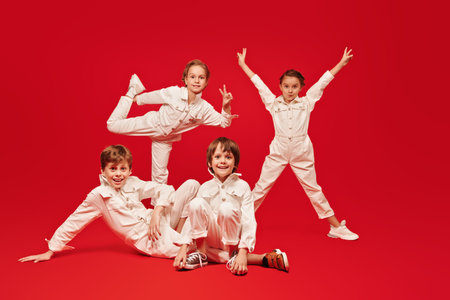 Happy childhood. Cheerful kids in white overalls posing together on a red background. Kid's fashion.