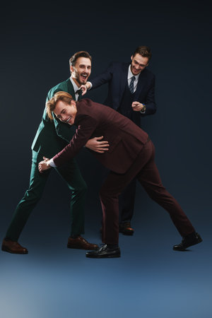 Three friends. Men's fashion. Three handsome men in elegant suits fight each other for fun. Dark...
