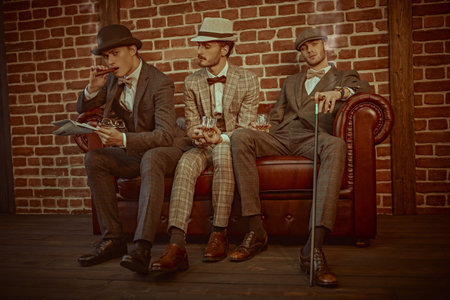 Three handsome men in elegant suits spends time in the men's club with cigars and whiskey. Luxury...