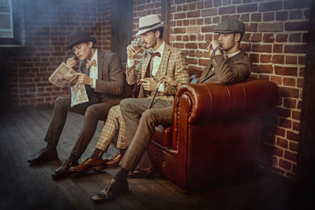 Men's beauty, fashion. Three handsome men in elegant suits spends time in the men's club with cigars and whiskey. Luxury lifestyle.の写真素材