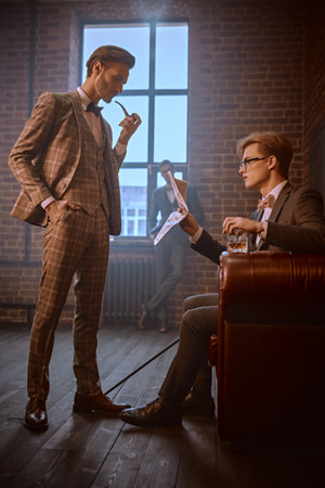 Handsome men in elegant suits spends time in the men's club with cigars and whiskey. Luxury lifestyle. Men's beauty, fashion.の写真素材