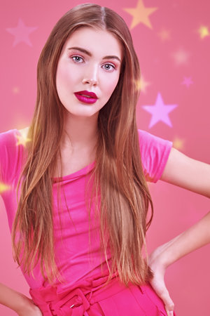 Cute girl teenager in a pink t-shirt posing on a pink background. Youth style. Cosmetics and make-up.の写真素材