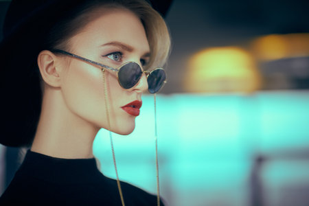 Close-up portrait of a fashionable young woman in modern sunglasses and hat in interiors. Beauty,...
