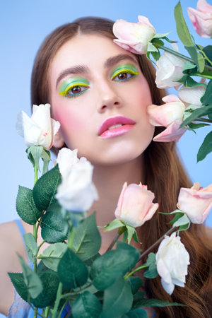 Beauty and flowers. Portrait of a tender young woman with bright colorful make-up and roses on a blue background. Make-up and cosmetics.の写真素材