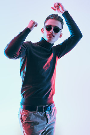 Fashion shot. Handsome young man in a dark gray pullover and modern black sunglasses. Men's accessories, optics. Studio portrait.の写真素材