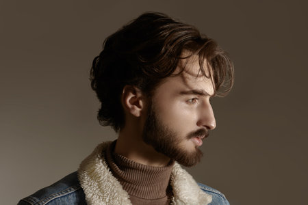 Men's beauty and hairstyle. Portrait of a handsome man with wavy dark hair and a beard on a gray background.の写真素材