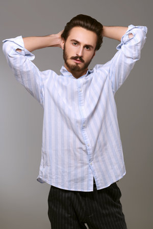 Men's beauty and hairstyle. Handsome brunet man posing at studio in light shirt and trousers. Men's fashion.の写真素材
