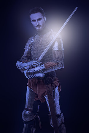 Portrait of a medieval knight with sword and armor on a black background.の写真素材