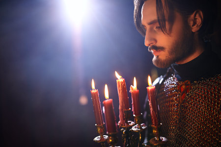 Close-up portrait of a medieval knight in armor standing with candles in the castle.
