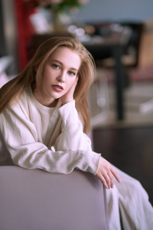 Portrait of a beautiful blonde girl having a rest on a sofa in her cozy living room. Happy life, happy people concept.の写真素材