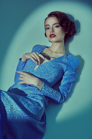 Stunning young woman in a long elegant dress and with hair and makeup in the style of the 20s posing in the circle of light. Light and shade.の写真素材