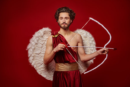 Valentine's Day concept. Portrait of the God of love - Cupid with bow and arrow on a red background.の写真素材