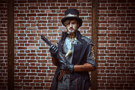 Portrait of a courageous steampunk male warrior with a gun on a brick wall background. World of steampunk.の写真素材