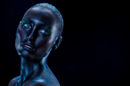 Body art project. Portrait of a beautiful fashion model woman with black painted skin and sparkling glitter makeup. Black background with copy space. Makeup and cosmetics.の写真素材
