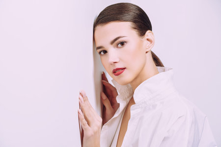 Summer fashion. Elegant young woman in light summer clothes poses at studio by the white wall. Copy space.の写真素材