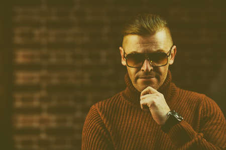 Handsome mature man in sunglasses over brick wall background. Optics style for men.の写真素材