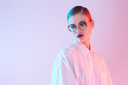 Portrait of a beautiful young woman in elegant glasses and white shirt on blue background. Copy...