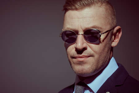 Close up portrait of a respectable mature man in a suit and sunglasses on a dark background. Businessman portrait. Copy space.の写真素材