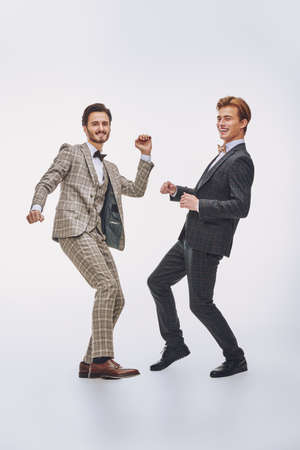 Men's fashion and accessories. Full length portrait of a handsome young dancing stylish guys in classic three-piece suit posing in a motion on a white background. Dancing gentleman.の写真素材