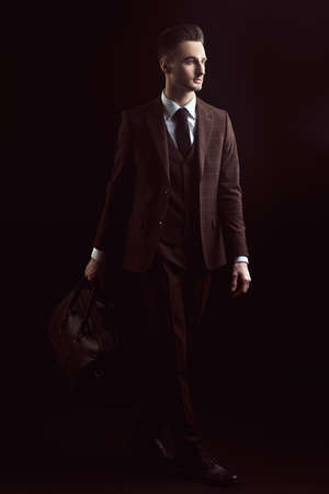Full length portrait of a handsome man in elegant classic suit and tie posing with leather bag on a black background. Business style. Men's fashion, accessories.の写真素材