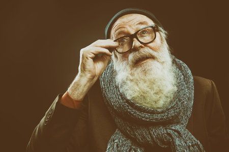 Portrait of a positive modern old man with a white beard and glasses looking up. Old age concept....