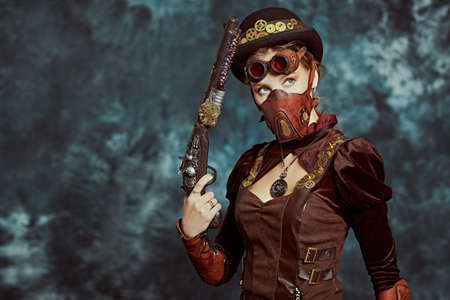 Steampunk concept. Portrait of a beautiful confident steampunk girl with a gun on a vintage background.の写真素材