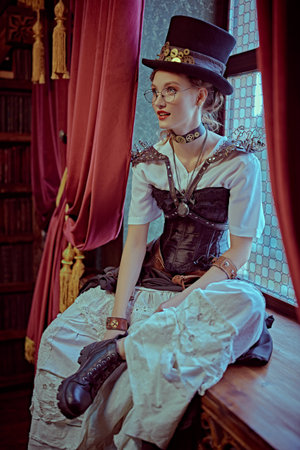 Portrait of a charming steampunk lady sitting on a windowsill in a room with Victorian vintage interior.の写真素材