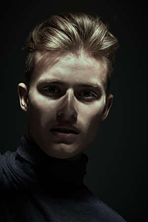 Close up portrait of a handsome man posing in studio in light and shadows on black background. Men's beauty.の写真素材