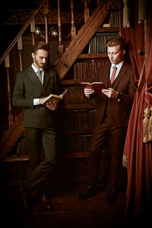 Portrait of two handsome young men in elegant classic suits reading books in a luxury apartments in the men's club. Men's beauty, fashion.の写真素材