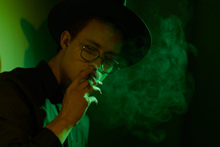 Portrait of a handsome young man smoking a cigarette and surrounded by smoke. Studio portrait in...