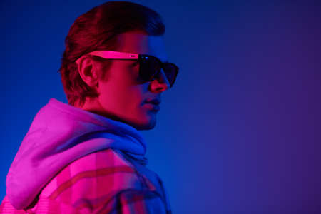 Modern young man in a plaid flannel shirt and a hoodie posing at studio in mixed color light. Youth fashion. Casual clothes style.の写真素材