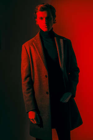 Portrait of an elegant male model posing in fashionable clothes at studio in red light. Fashion shot.の写真素材
