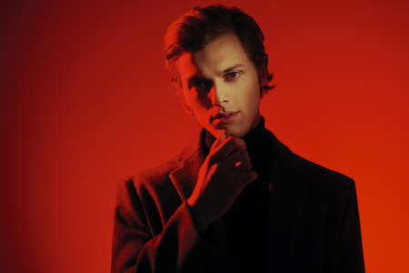 Portrait of a handsome young man in elegant clothes posing at studio in red light. Men's style. Copy space.の写真素材