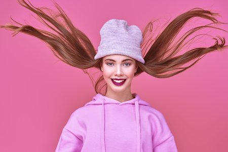Youth fashion. Joyful teen girl in a pink sweatshirt and a hat jumping in front of the camera and...