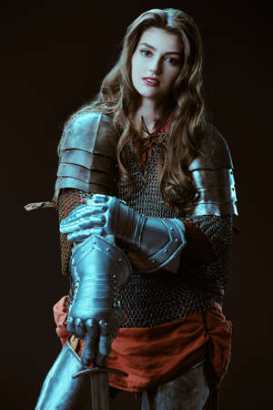 A beautiful noble warrior woman in chainmail and plate armor poses on a black background. Medieval knight. Studio portrait.の写真素材
