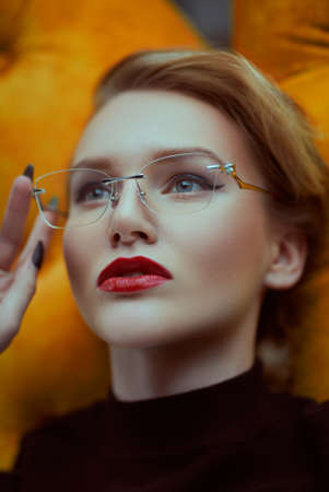 Attractive lady in elegant glasses lying on a yellow couch. Beauty, fashion. Optics style.の写真素材