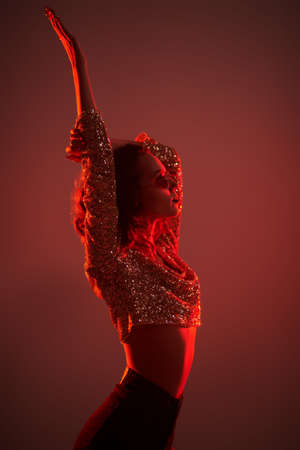 Portrait of a modern girl in sparkling top and jeans with stylish glasses alluring in red ligh. Night party. Disco style.の写真素材