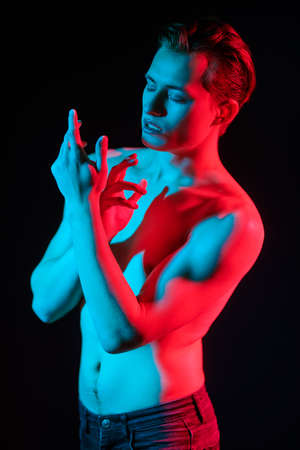 Art portrait of a handsome athletic young man posing with naked torso in red and blue light. Man's beauty and health. Art portrait.の写真素材