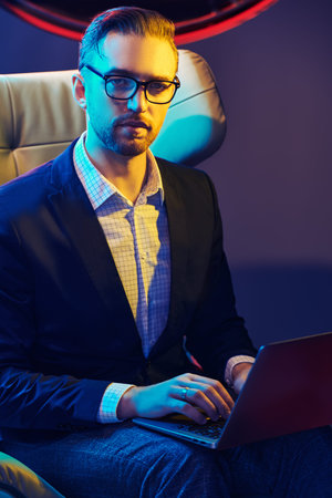 Portrait of a successful businessman in smart casual clothes and glasses uses his laptop sitting on...