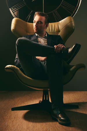 Handsome middle-aged man in elegant clothes and stylish shoes sits in a luxury leather armchair. Successful manager concept. Men's fashion.の写真素材