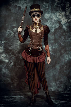 Full length portrait of beautiful steampunk lady holding gun over vintage background. Science adventure novel.の写真素材