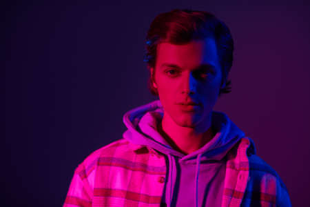 Modern young man in a plaid flannel shirt and a hoodie posing at studio in mixed color light. Casual clothes style. Youth fashion.の写真素材