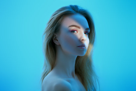 Portrait of an attractive blonde girl with fresh makeup in pink colors on a blue background in the shadows. Beauty woman. Body and hair care cosmetics.の写真素材
